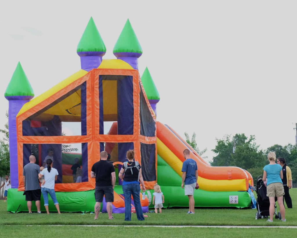 Jumping JS Party Rentalz, Families enjoy a colorful inflatable bounce house with slide at an outdoor event.